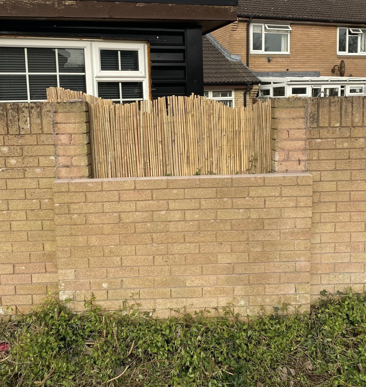 A buff brick boundary wall carrying a close-board fence