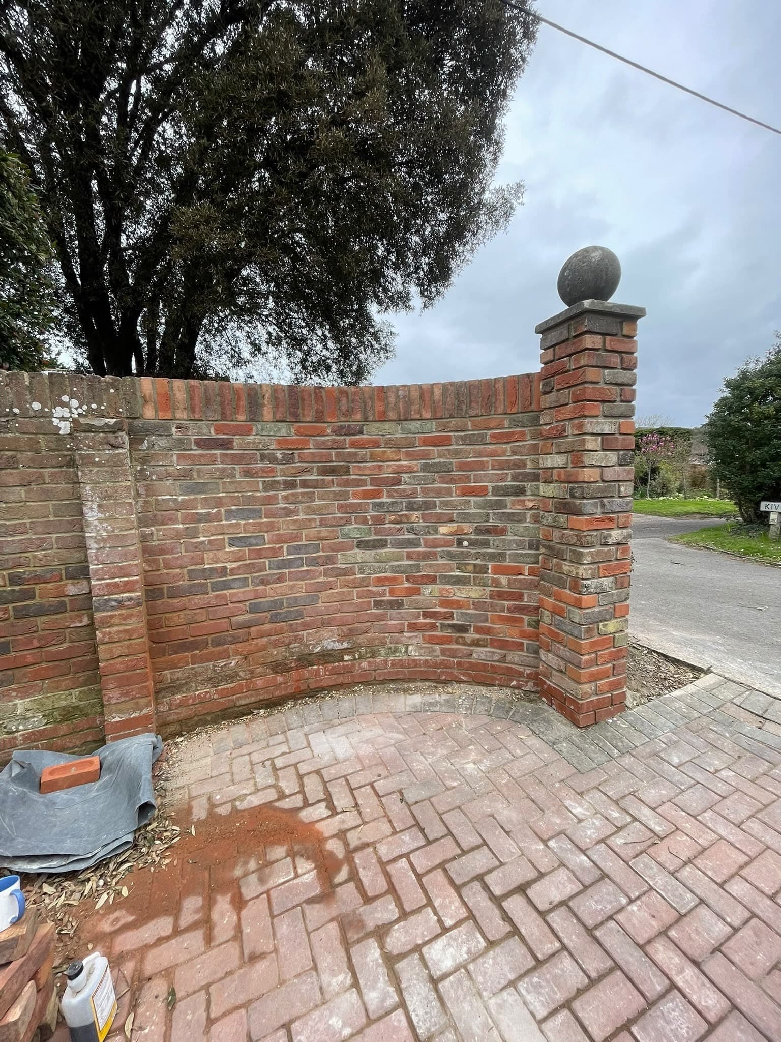 A curved brick wall beside a herringbone block driveway