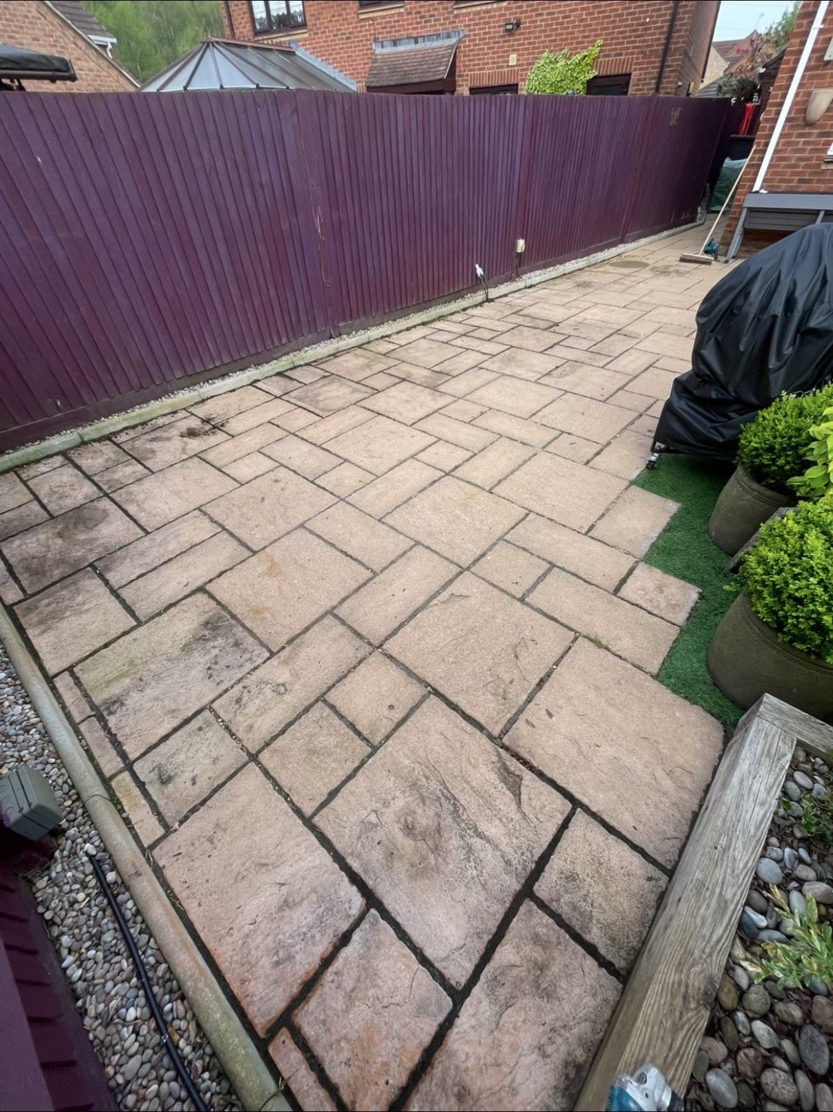A block paved patio laid up to a painted boundary fence
