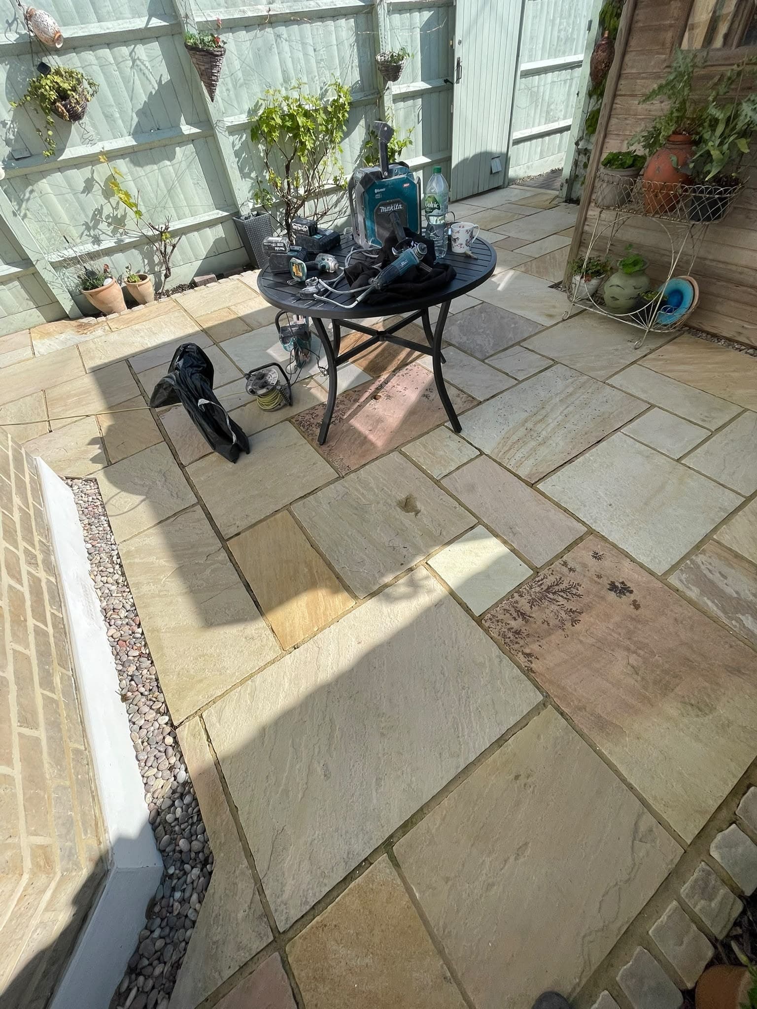 A buff sandstone patio with a table set out in the shade