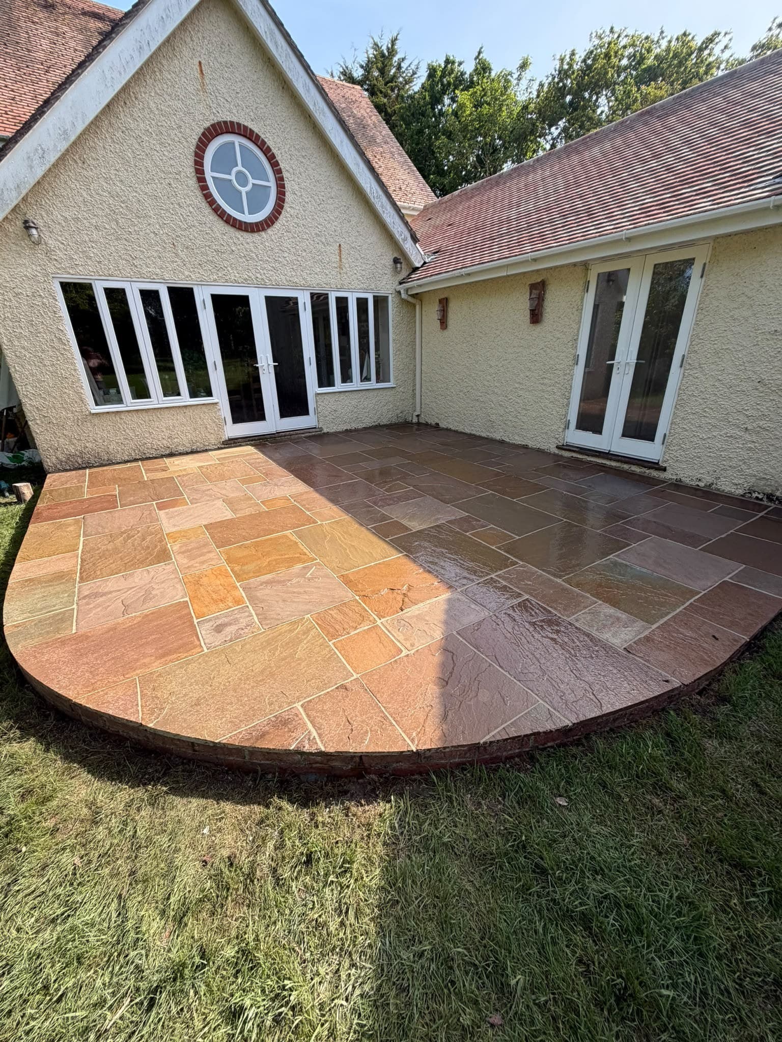A curved Indian sandstone patio behind a rendered house, freshly repointed